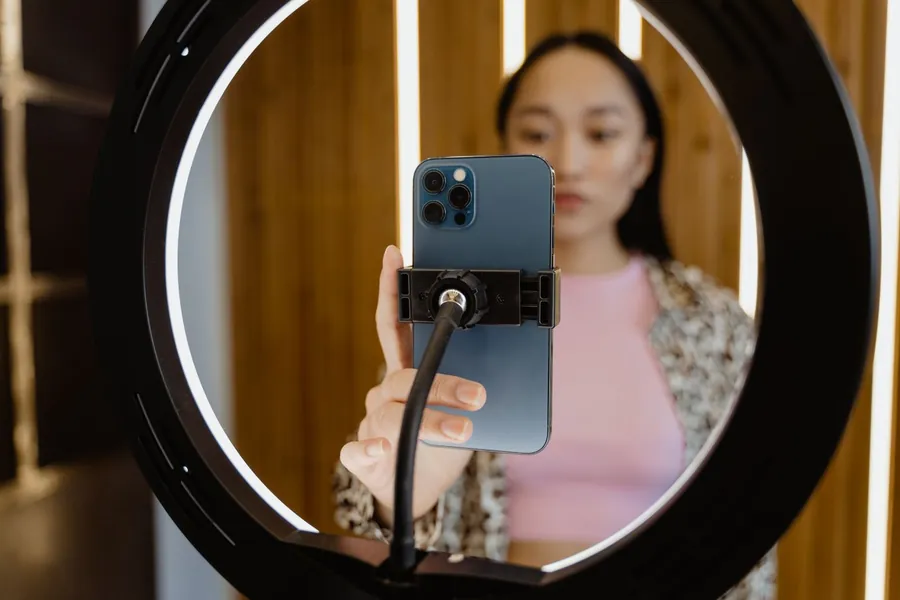 A person recording a video on a smartphone mounted in a ring light