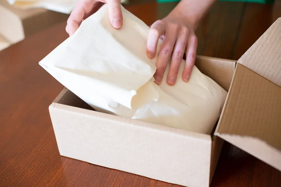 Hands packing an order into a cardboard shipping box